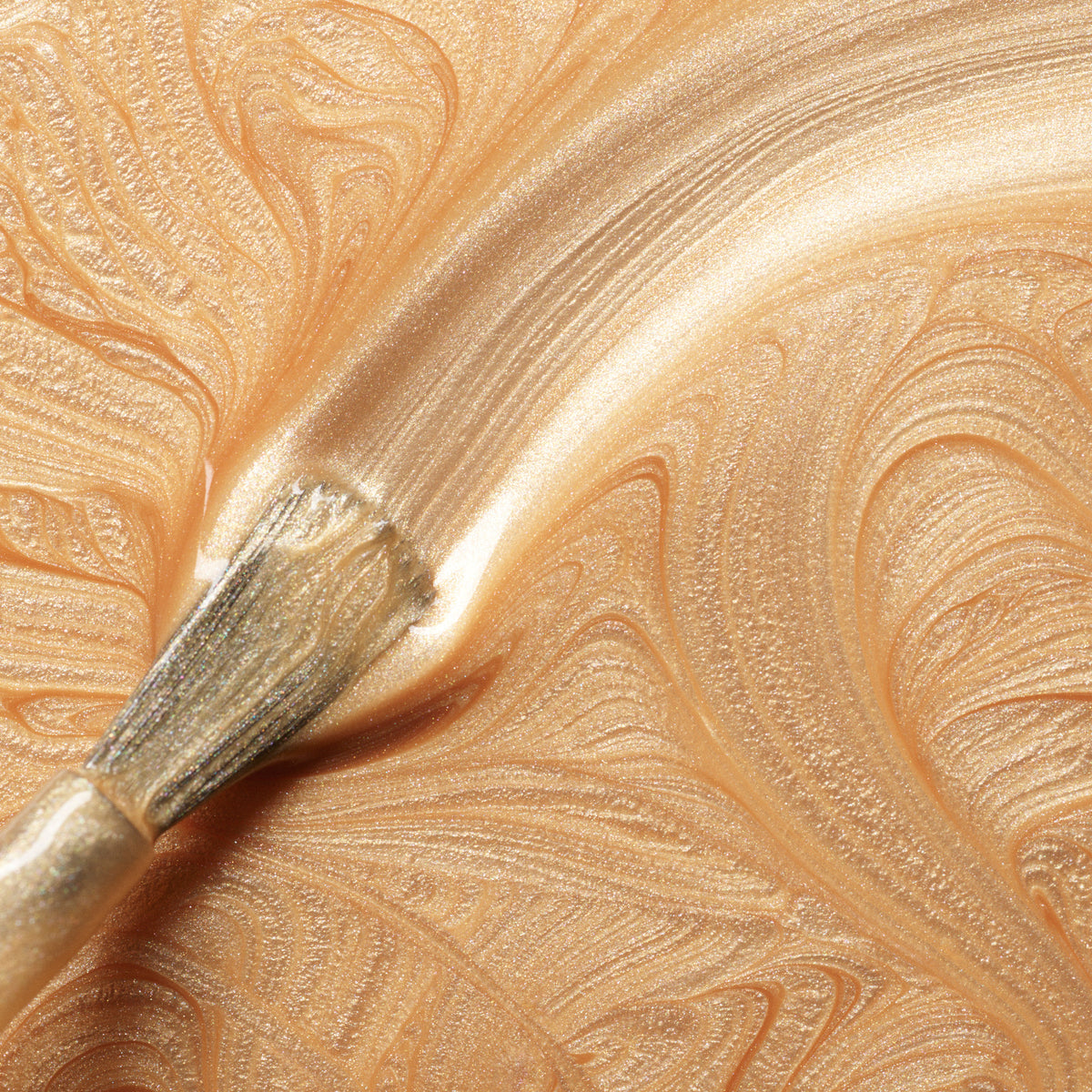 A close-up of a brush spreading Manucurist’s Gold Sand, creating swirling, shimmery patterns with a textured surface reminiscent of iridescent nail polish.