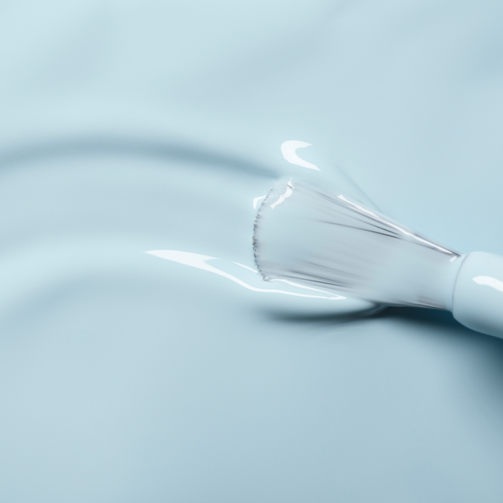Gros plan sur un pinceau Manucurist appliquant le vernis à ongles Light Blue sur une surface lisse.