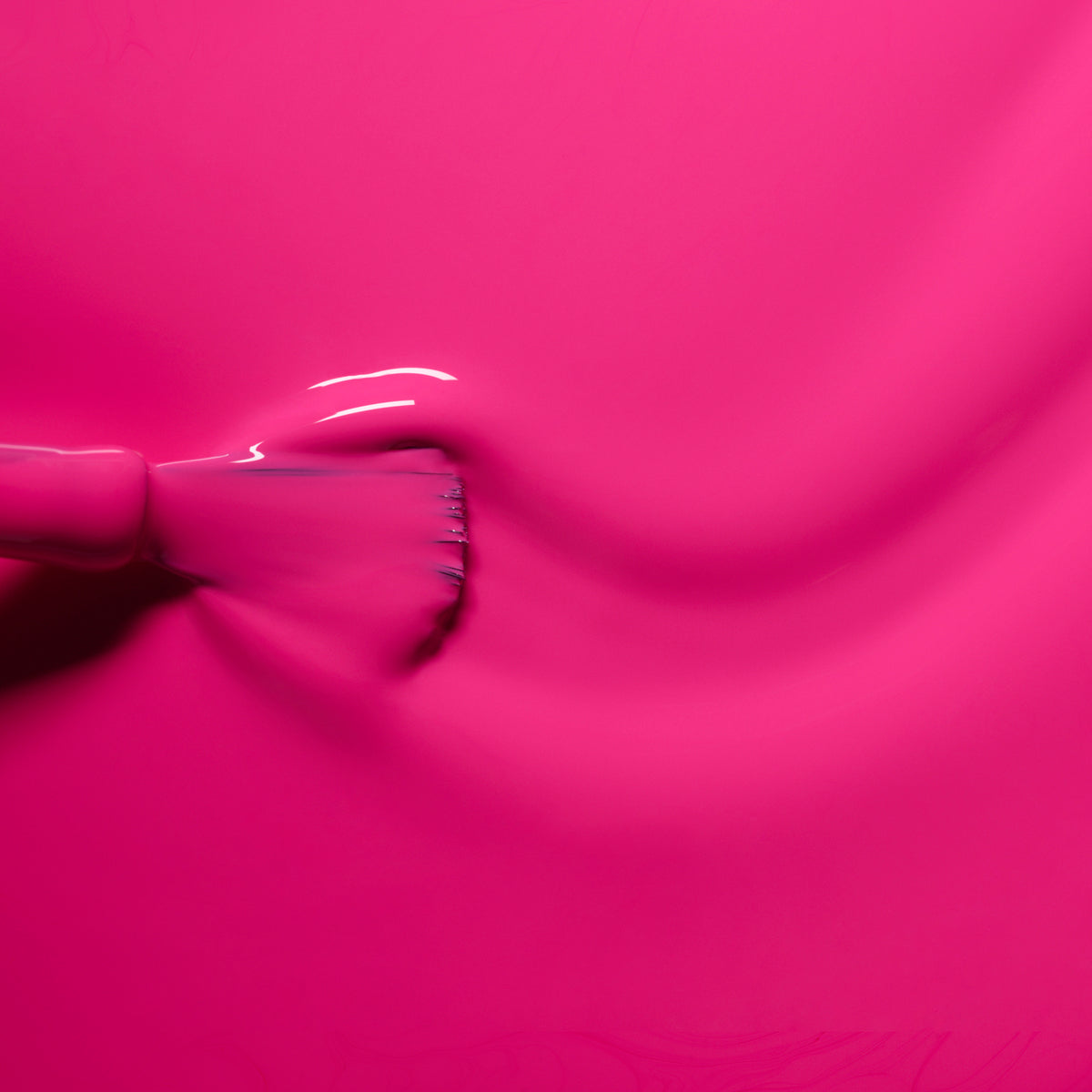 Gros plan d’un pinceau étalant Pétula de Manucurist, un vernis à ongles rose vif, sur une surface lisse, révélant une finition brillante, des sous-tons bleus et des traces de pinceau visibles.