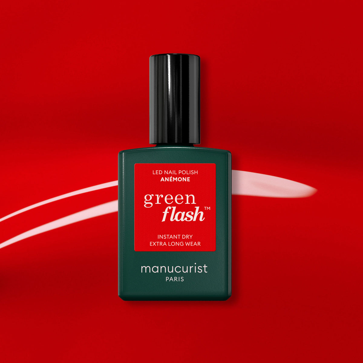 A bottle of Manucurist Anémone gel polish stands out on a bold red background with a white brushstroke. This light red shade from Manucurist Paris pops with vibrant color and shine.