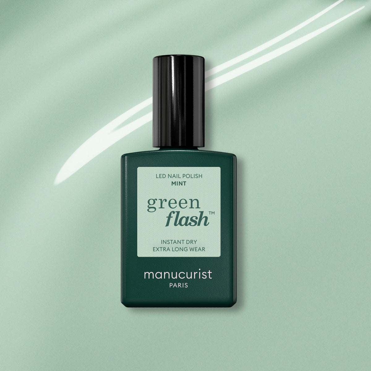 A bottle of Manucurist Mint Green Flash gel polish is displayed on a mint green background with a white swoosh. The dark green bottle features a black cap and a pastel green label.