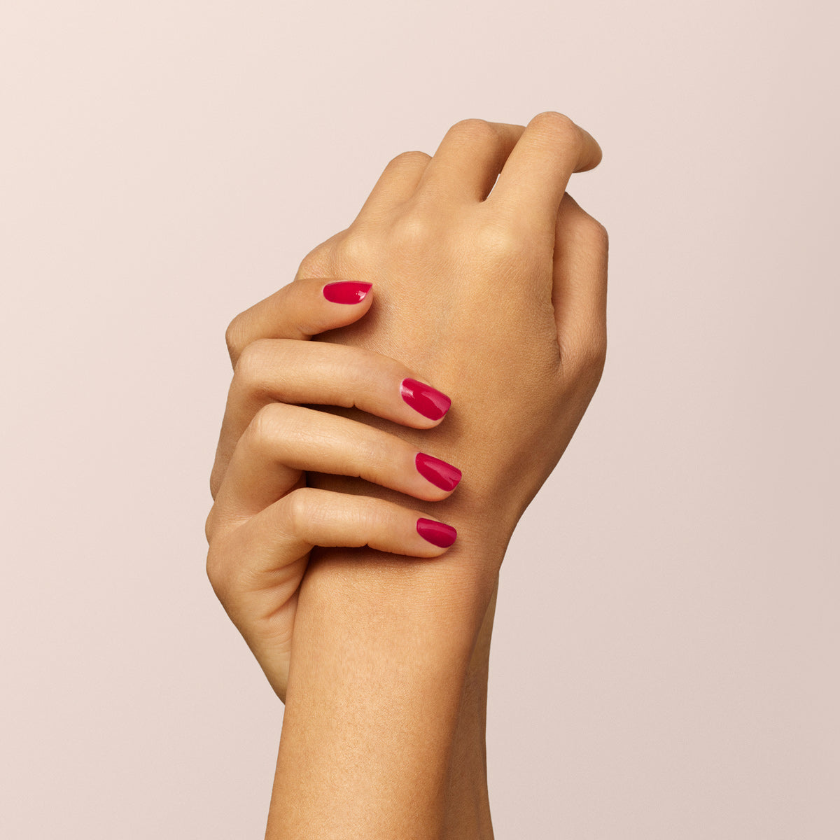 A close-up of two hands with neatly manicured nails painted in Manucurist’s Pomegranate, posed gracefully against a soft beige background.