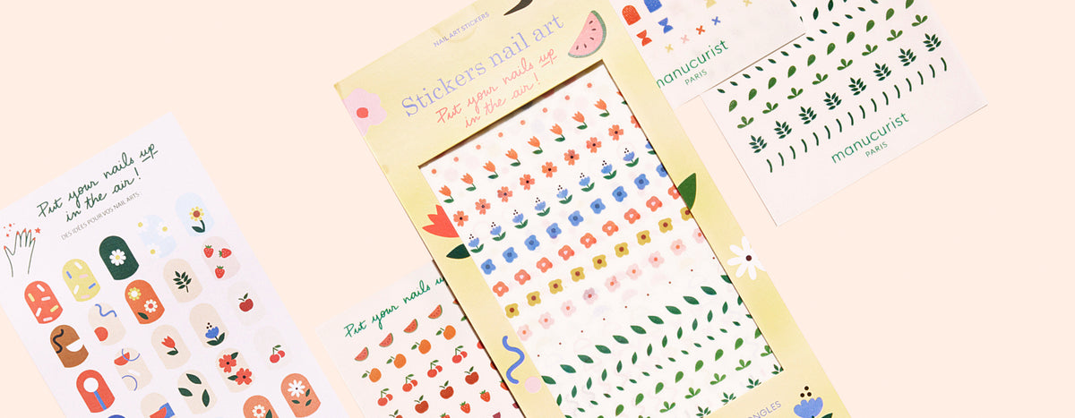 A set of colorful nail art stickers featuring flowers, leaves, and abstract designs, displayed in packaging and on sheets against a light peach background.