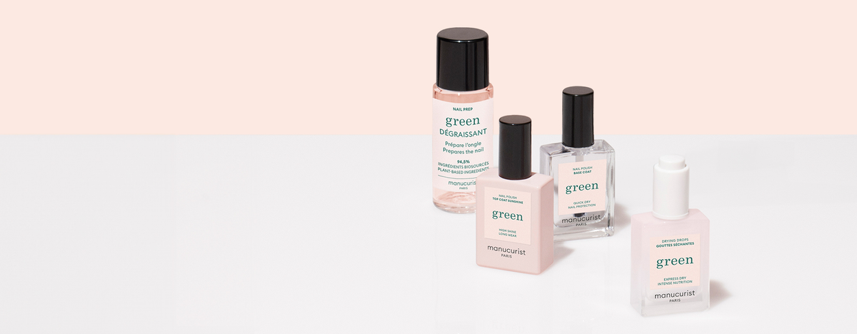 Four bottles of manicure products labeled “green” from the brand Manucurist are arranged on a white surface with a light pink background.