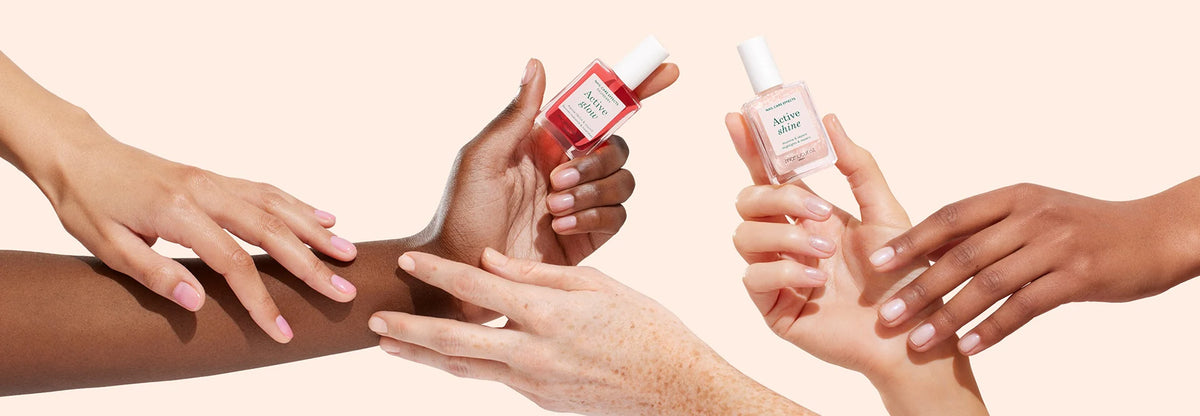 Several hands with different skin tones display manicured nails while holding bottles of nail polish and nail treatment against a light peach background.