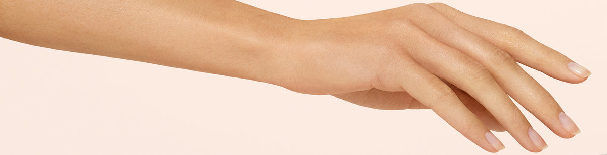 A close-up of a persons hand and forearm against a pale background, with fingers gently extended and nails neatly trimmed.