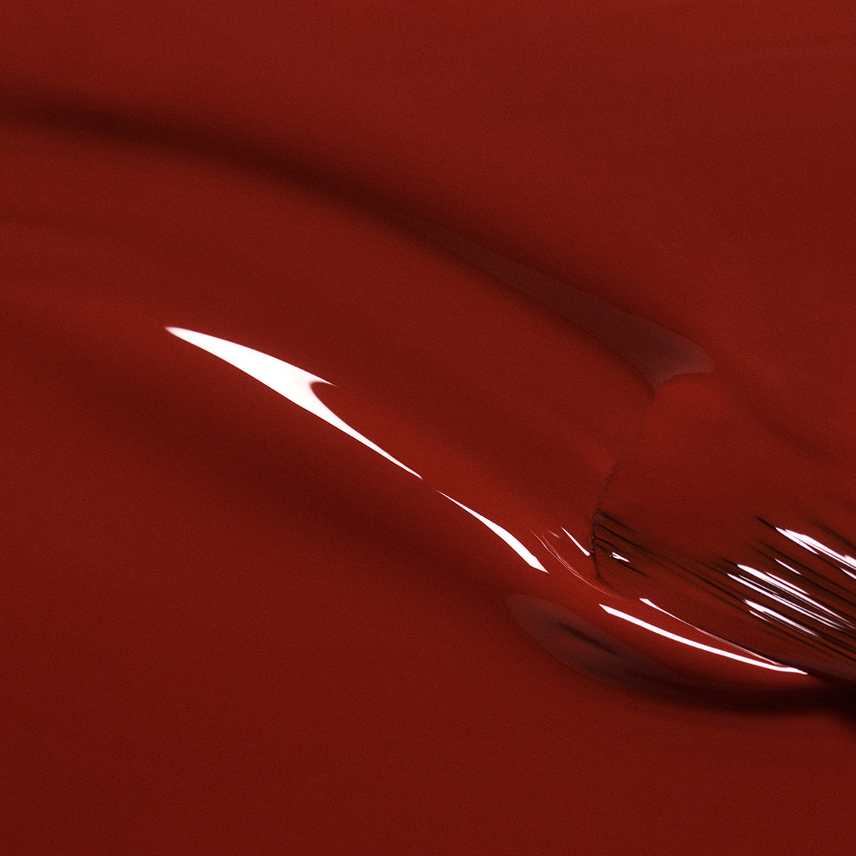 Gros plan de Bohème par Manucurist — une surface rouge brillante et lisse aux sous-tons bruns et aux reflets courbes, évoquant un vernis rouge pour un rendu abstrait et fluide.