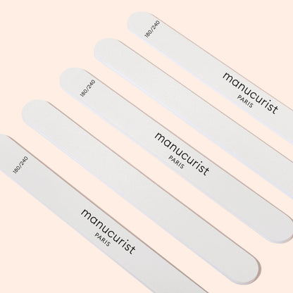 Five Manucurist-us 180/240 emery boards for fragile nails are arranged diagonally on a light beige background, ideal for gently shaping brittle or sensitive nails.