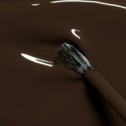 A close-up of a Manucurist Mocha brush dipped in smooth, glossy dark brown nail polish, with bright reflections highlighting the bristles and polish surface.