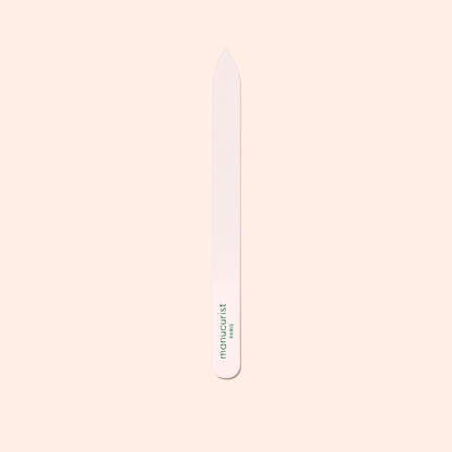 The Manucurist-us Glass Nail File features a pointed tip and "manucurist" in green near the base, shown vertically on a pale beige background.