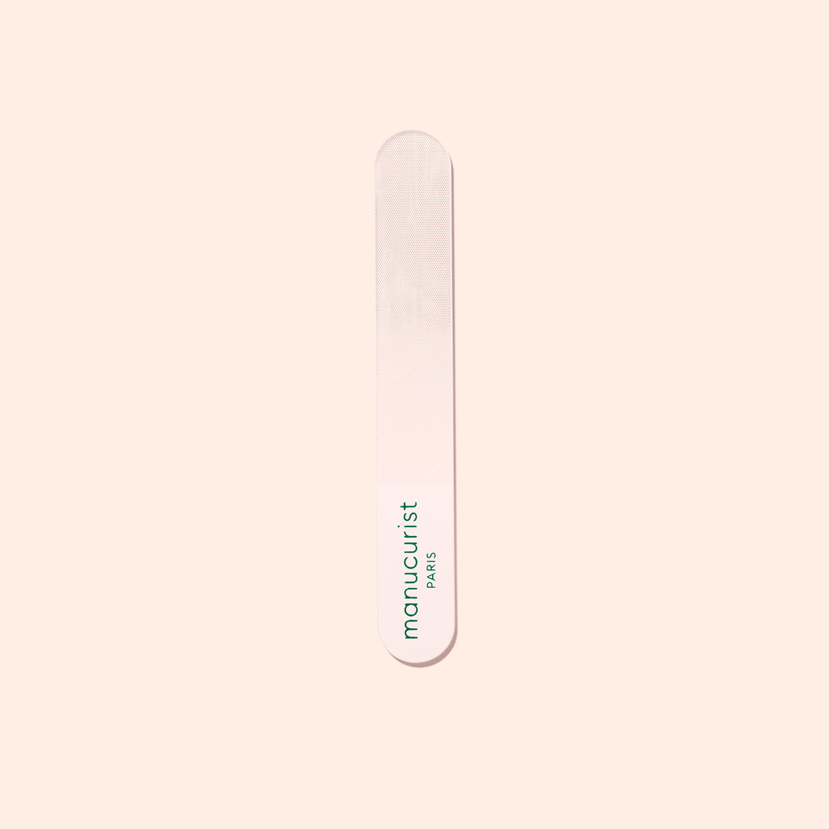 A Manucurist-us Glass Polisher with rounded ends rests on a pale surface. “Manucurist-us” is printed vertically in green, making it ideal for gently enhancing the natural shine of your nail plate.