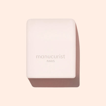 A pale pink rectangular Mani Helper soap bar from Manucurist US, embossed with the logo, rests on a beige background with a soft shadow—ideal for prepping hands before a perfect manicure or nail polish application.