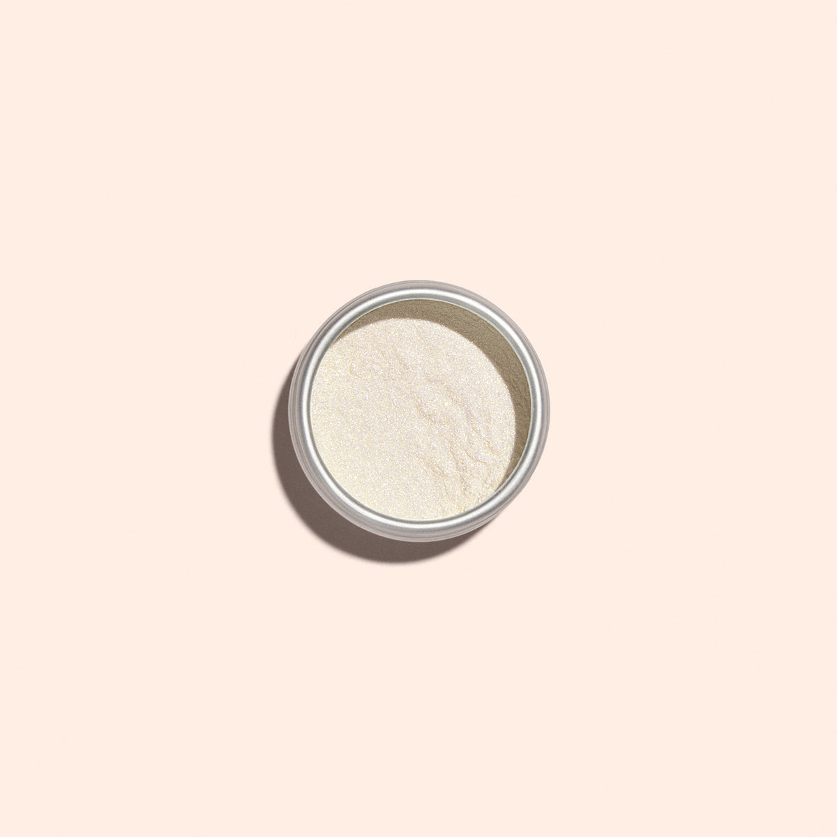 Une petite boîte métallique de Golden Glazed Effect Powder de Manucurist — une fine poudre blanc cassé qui donne aux ongles un scintillement doré nacré — est centrée sur un fond beige clair et projette une douce ombre vers la gauche.