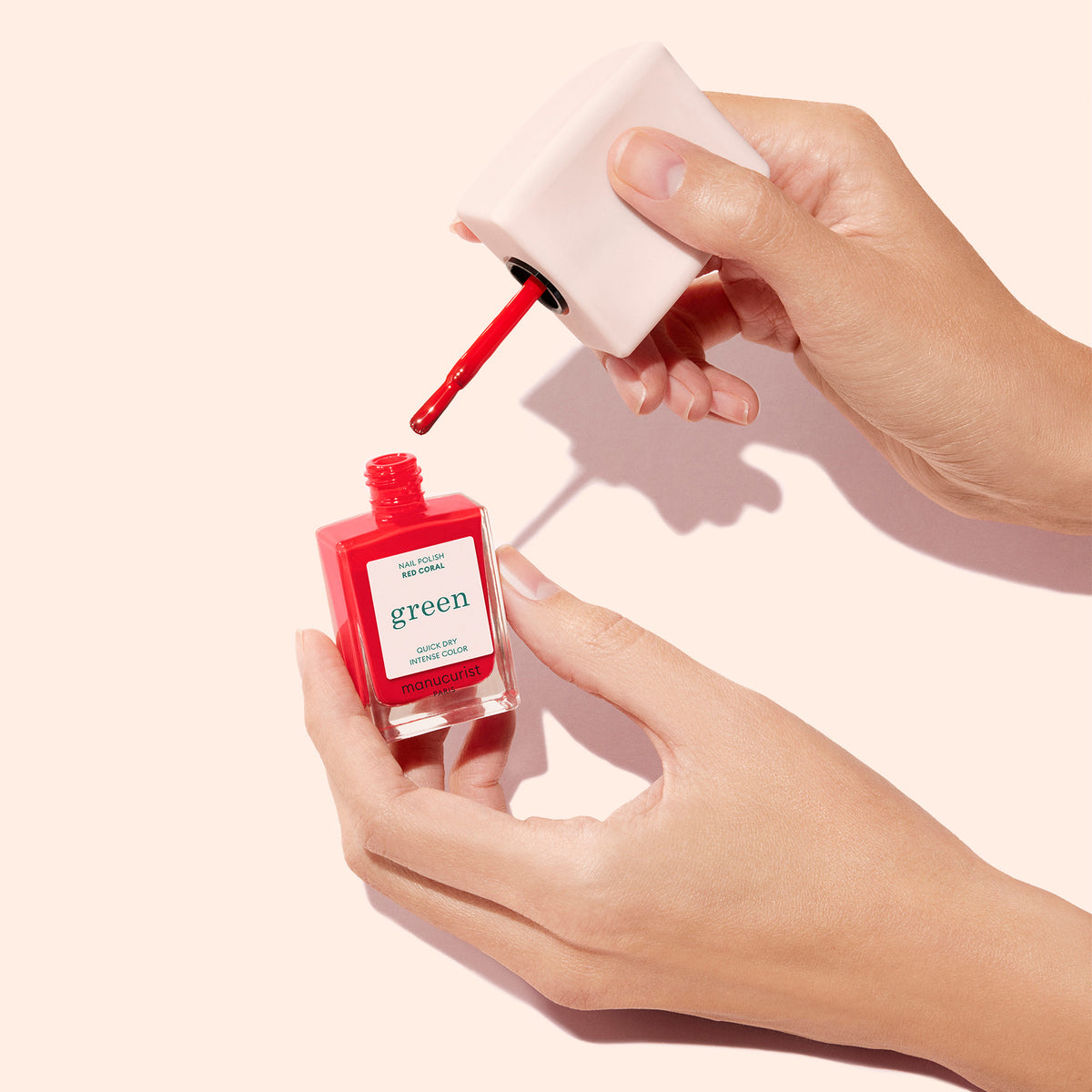A hand holds a square Mani Helper bottle by Manucurist US as another unscrews the cap with the brush applicator, highlighting flawless manicure technique against a light beige background.