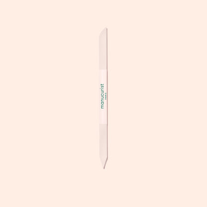 The Manucurist Glass Cuticle Pusher features a pointed tip and beveled edge for precise nail contouring, with "manucurist" in green on a white center section, displayed on a light beige background.