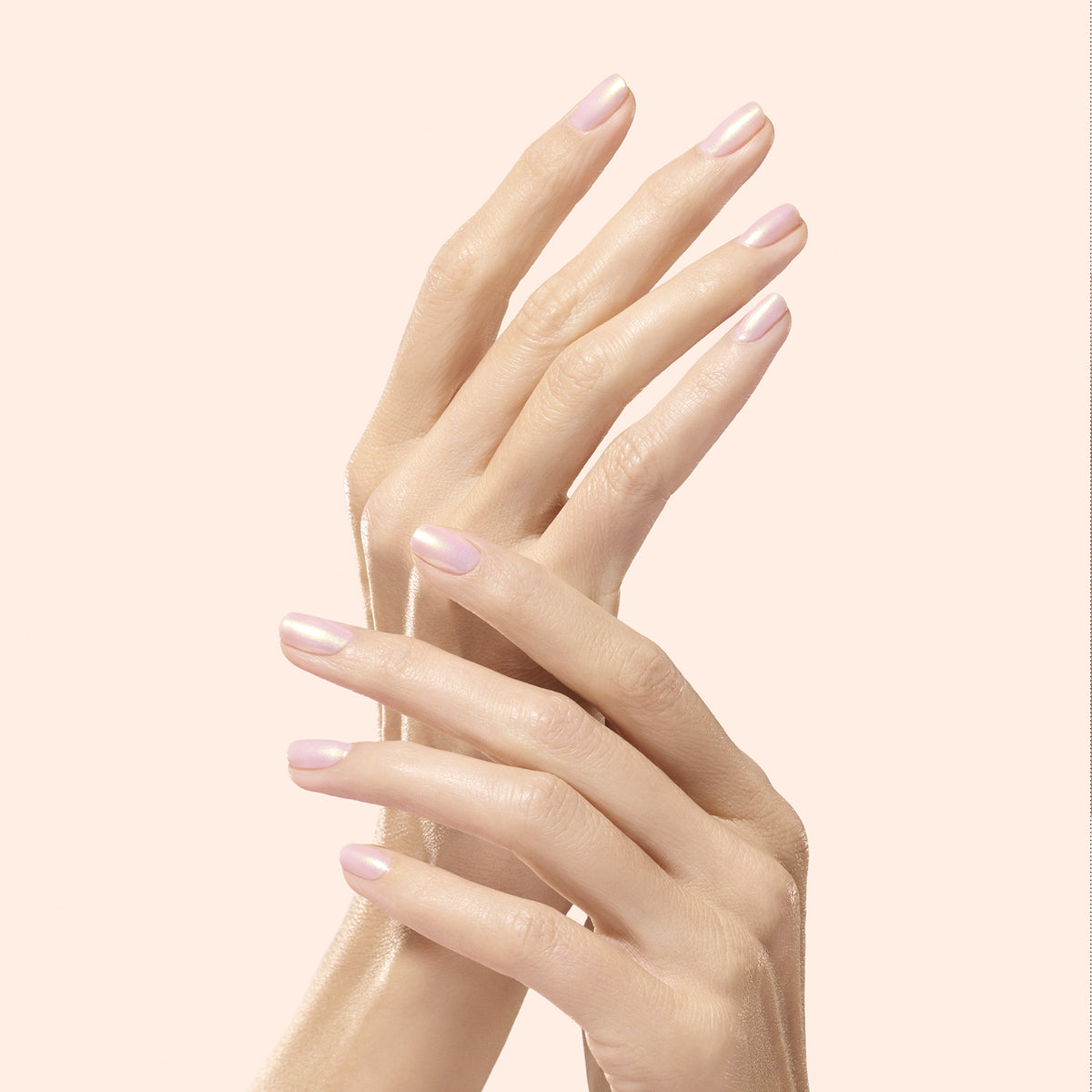 Deux mains aux ongles parfaitement manucurés et soigneusement limés, sublimés par la Glazed Effect Powder dorée de Manucurist, se frôlent délicatement, révélant une teinte rose pâle aux reflets or nacrés sur fond beige doux.