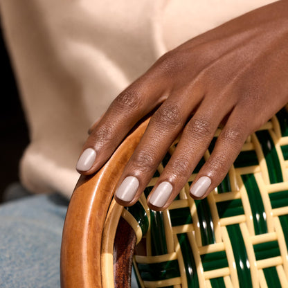 Une main aux ongles beige clair soigneusement manucurés, vernis avec "Tweed" de Manucurist, repose sur l&