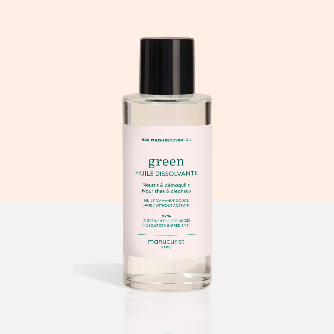 A clear bottle with a black cap contains Manucurist Nail Polish Removing Oil, a green, plant-based formula. The bottle features a light pink label with green text on a beige and white background.