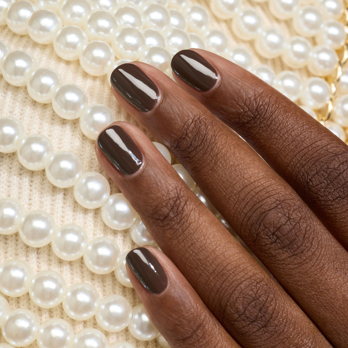 A hand with dark brown polished nails rests on a surface decorated with rows of white pearls.