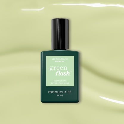 Un flacon de Manucurist Pistachio, un vernis gel LED vert pâle aux sous-tons jaunes, est présenté sur un fond vert clair brillant.