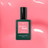 A bottle of Manucurist Pop Green Flash LED nail polish, a vibrant shade with orange undertones, rests on a glossy pink surface with reflected light, its black cap and green label standing out.