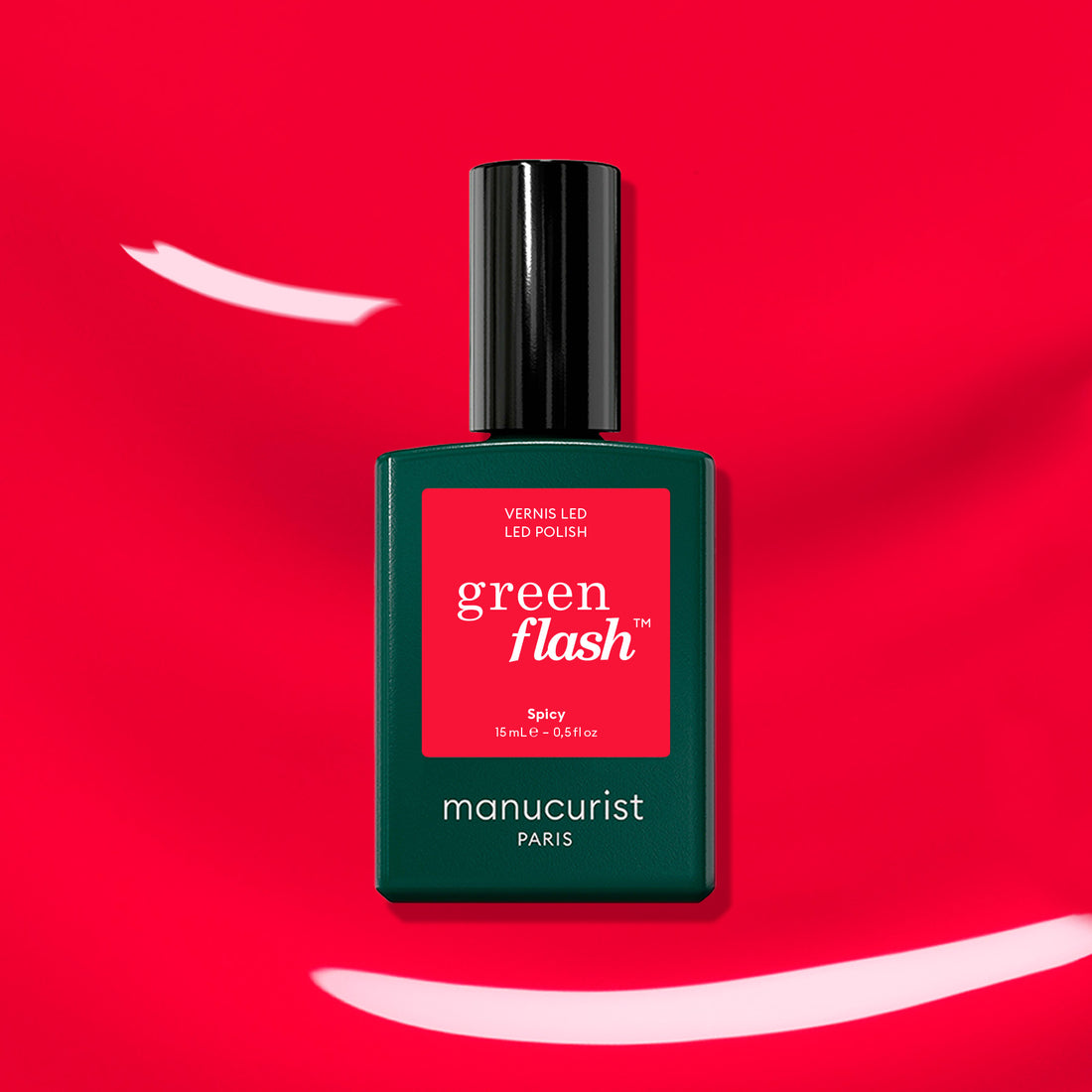 A bottle of Manucurist Spicy gel polish stands against a vibrant red background with white brushstroke accents. The dark green bottle, black cap, and red label highlight this bold pop red shade.