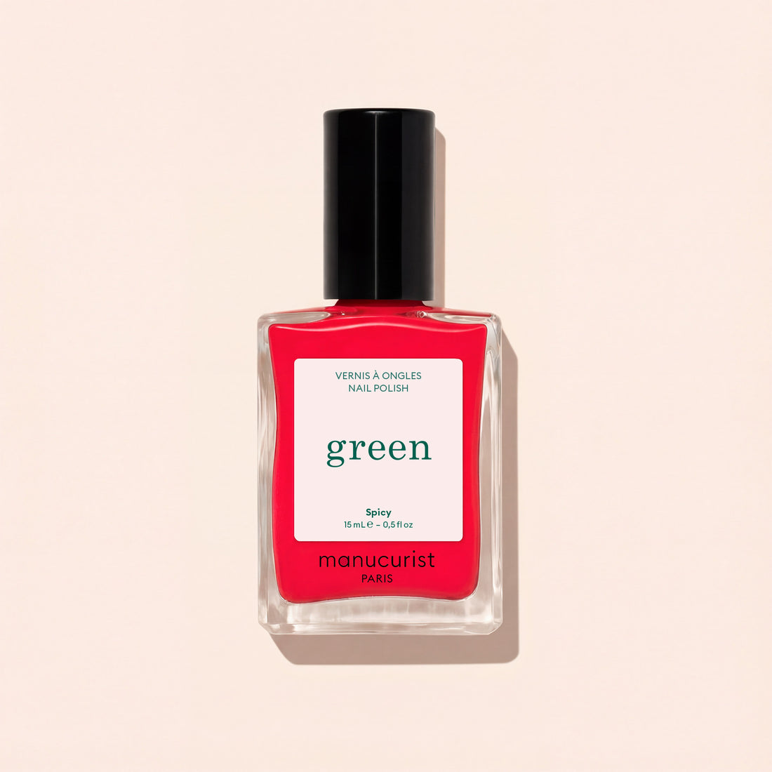 Un flacon de vernis à ongles Spicy de Manucurist, une teinte rouge pop aux sous-tons roses de la gamme Green™, avec un bouchon noir et une étiquette blanche, sur un fond beige clair.