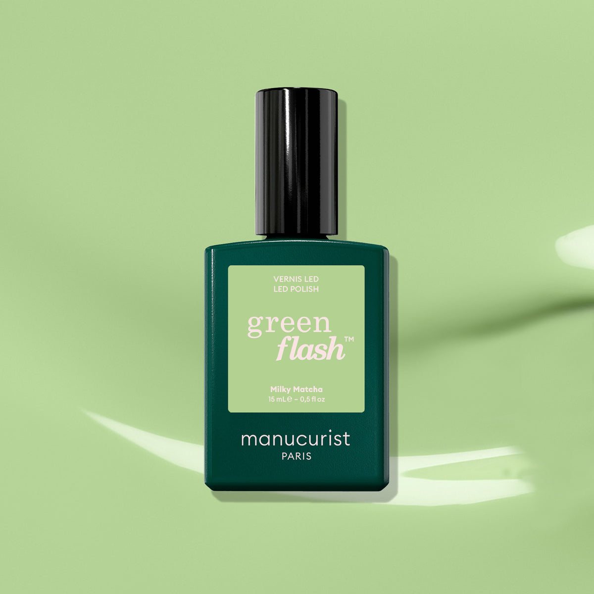 A dark green bottle of Milky Matcha by Manucurist—a creamy, milky matcha green gel polish—rests on a light green background with gentle shadows.