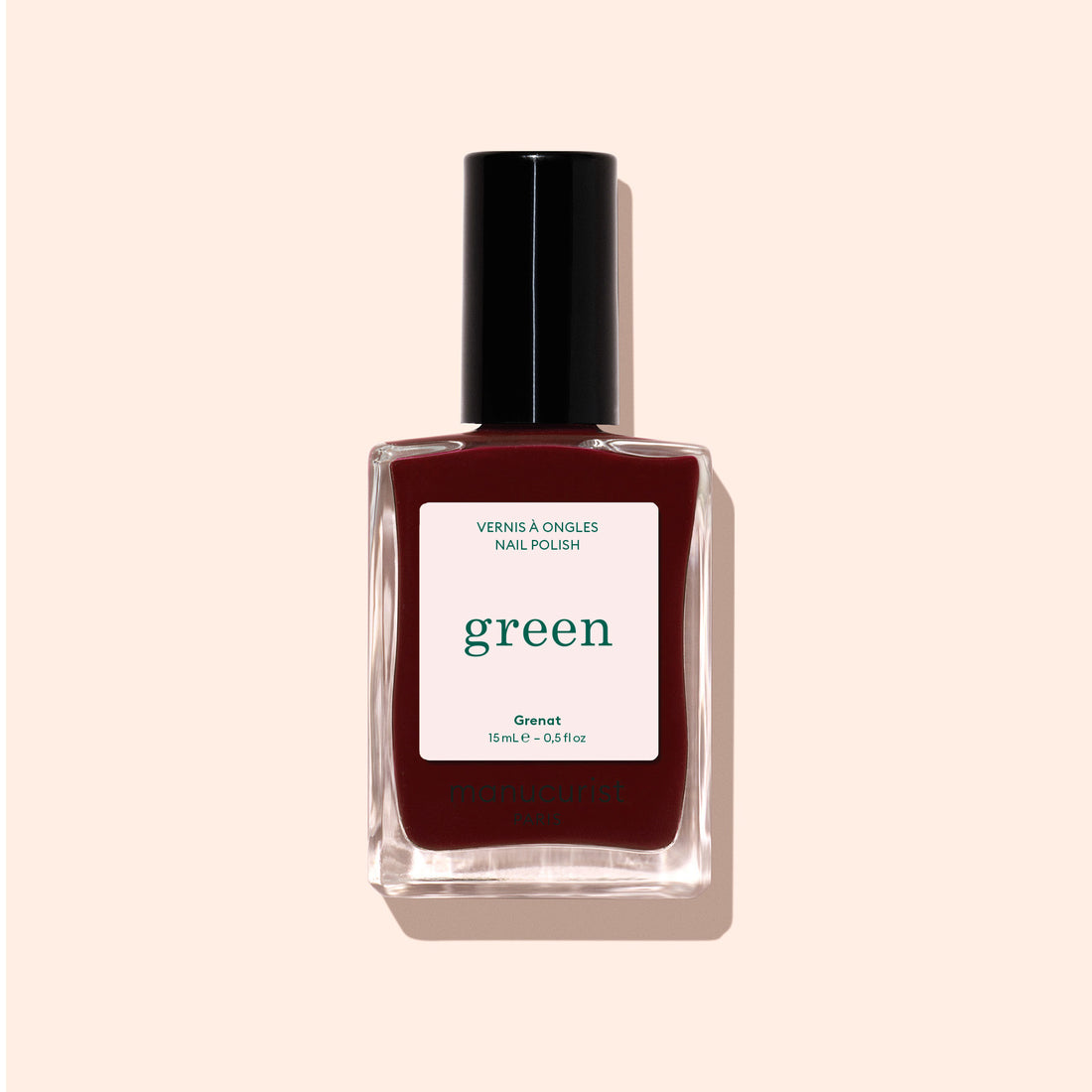 Un flacon de vernis à ongles Manucurist Grenat de la gamme Green, avec un bouchon noir, est présenté sur un fond beige clair. L’étiquette indique « green » et « Nail Polish », mettant en valeur cette teinte rouge marron terreuse.