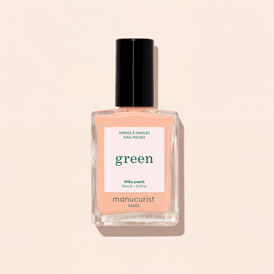 Un flacon de vernis à ongles Milky Peach de Manucurist repose sur une surface beige clair. Le flacon transparent, doté d&