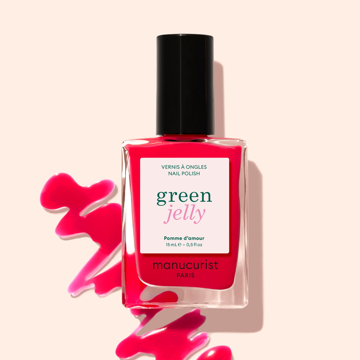 A bottle of Manucurist Pomme d'Amour Jelly nail polish, a bright red syrup-finish shade, is shown with spilled red polish on a light pink background.