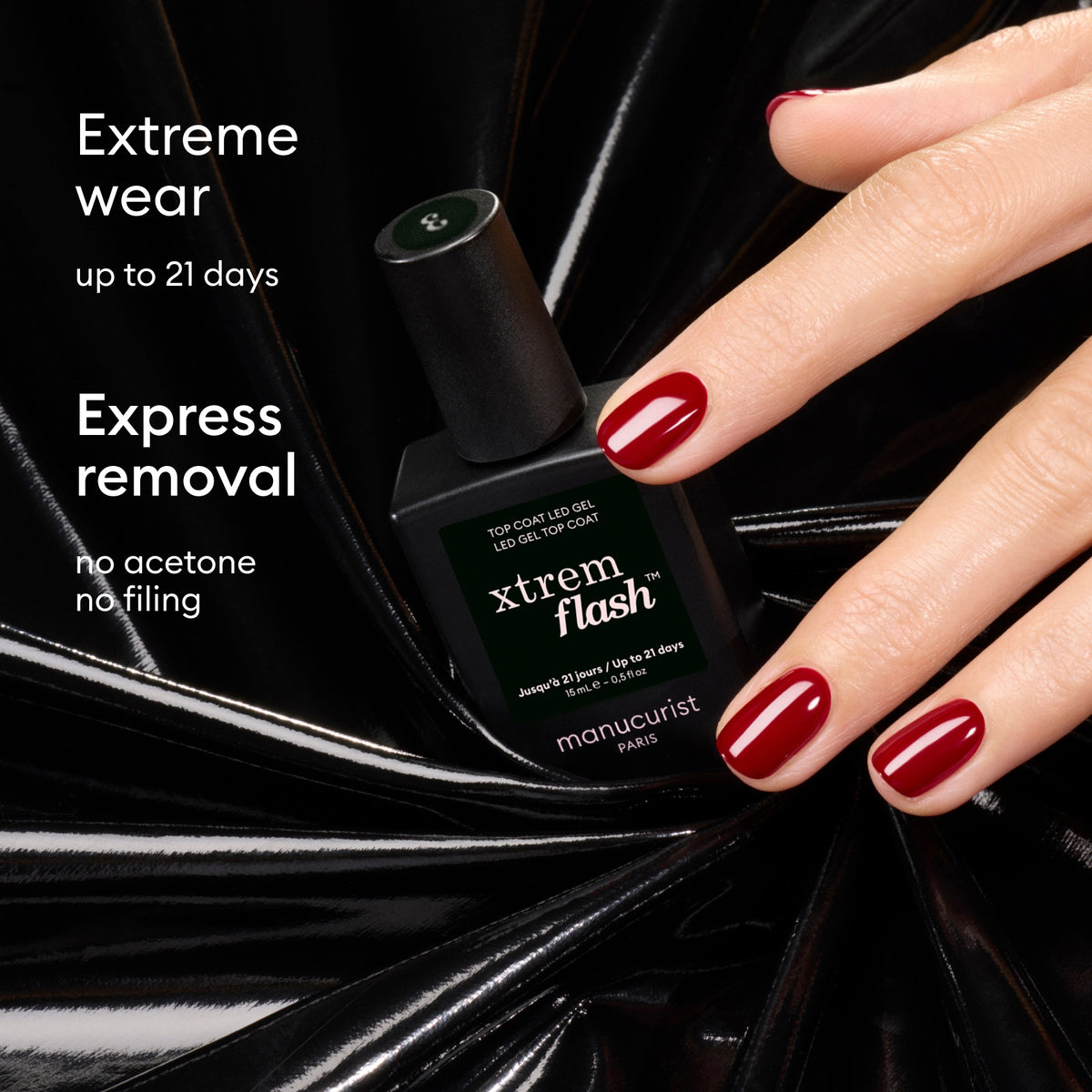 A hand with glossy red nails holds a black bottle of Manucurist Xtrem Flash™ Gel Top Coat against a shiny black background. Text reads: Flawless wear up to 21 days. Express removal—no acetone, no filing.