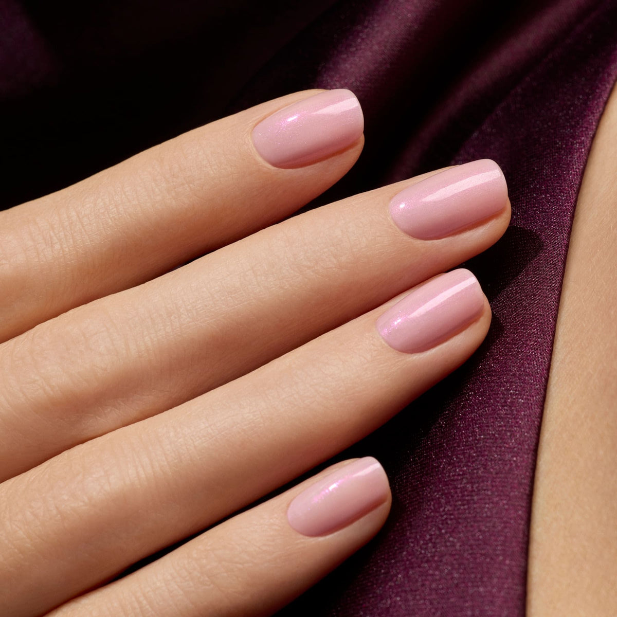 Gros plan sur une main aux ongles impeccablement manucurés avec Halo de Manucurist, un vernis gel mauve laiteux rose clair au fini brillant, posée sur un satin violet profond.