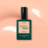 Un flacon de vernis LED Manucurist Milky Peach Green Flash™, une teinte gel pêche laiteuse aux tons beige orangé doux, présenté sur un fond pêche ponctué de reflets de lumière blanche.