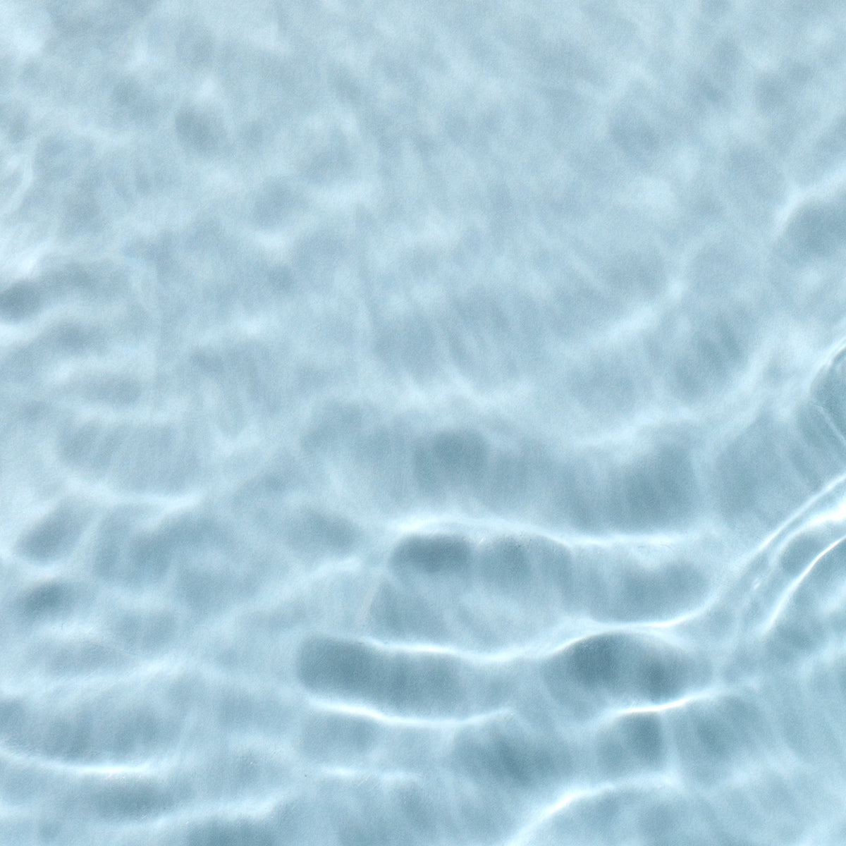 Sunlight creates wavy, rippling patterns on the surface of clear, light blue water. The texture is smooth, and the water appears calm and undisturbed.