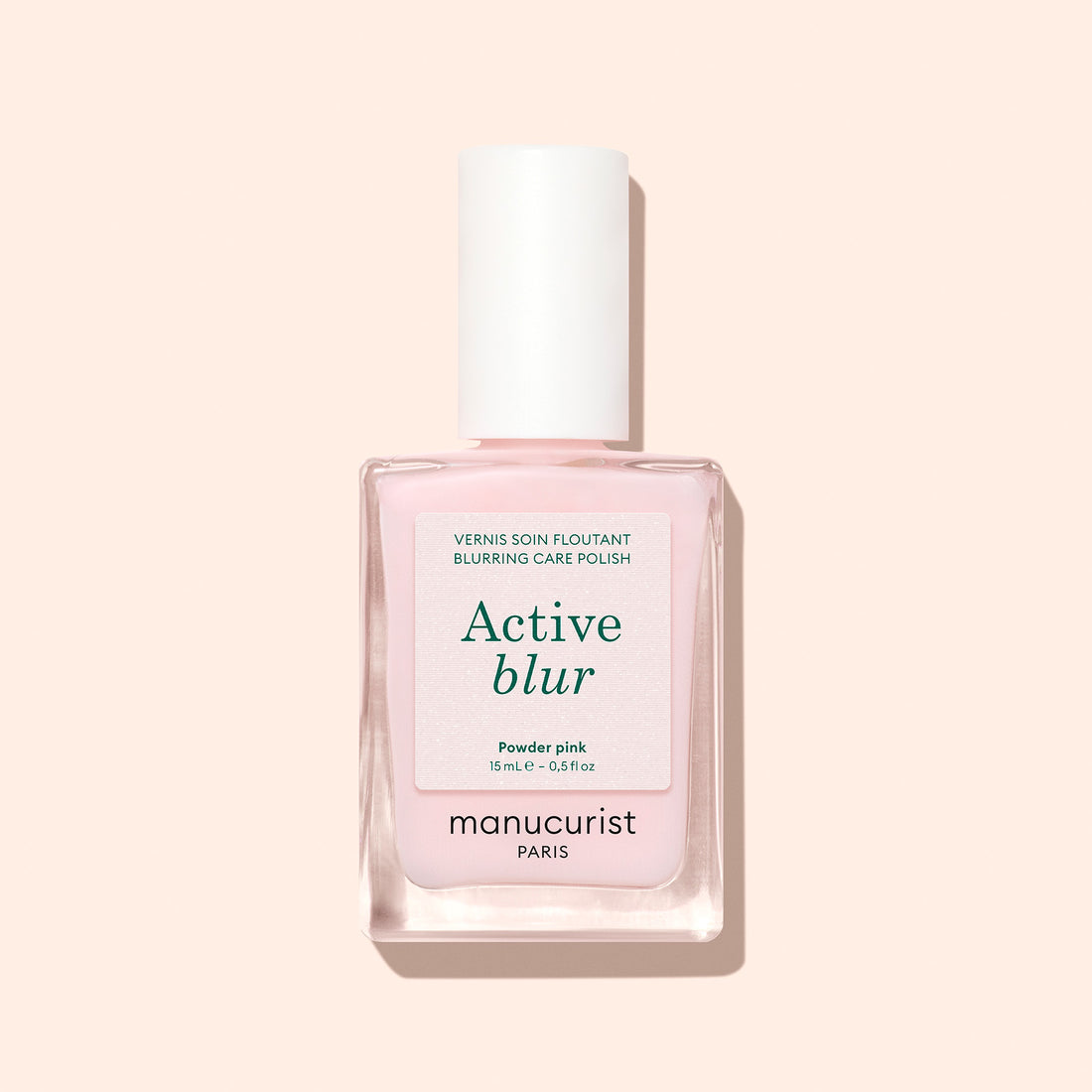 A bottle of Manucurist Active™ Blur nail polish in powder pink, showcasing a flawless matte finish and topped with a white cap adorned with a minimalist label, displayed against a light beige background.