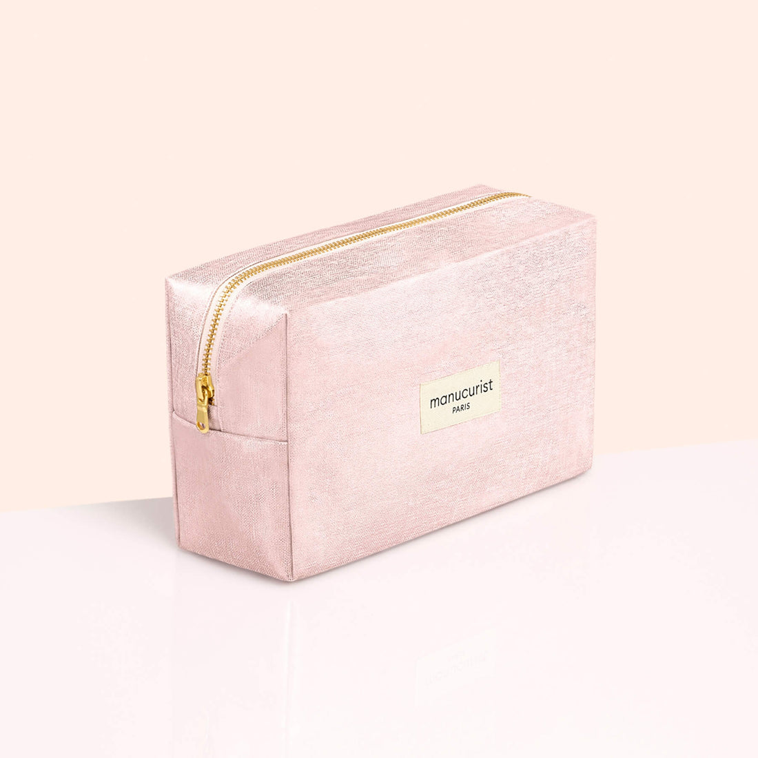 The Pink Lurex Pouch by Manucurist-us is a rectangular cosmetic bag in light pink with a shimmering finish, highlighted by a gold zipper and the Manucurist Paris label on the front. Set against a soft peach and white background, this pouch is perfect for storing your manicure essentials, effortlessly blending style and practicality for everyday glamour.