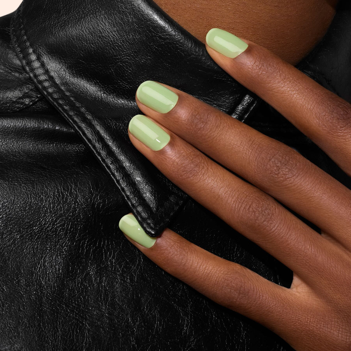 A hand with Manucurist Milky Matcha green gel polish rests on the collar of a black leather jacket.
