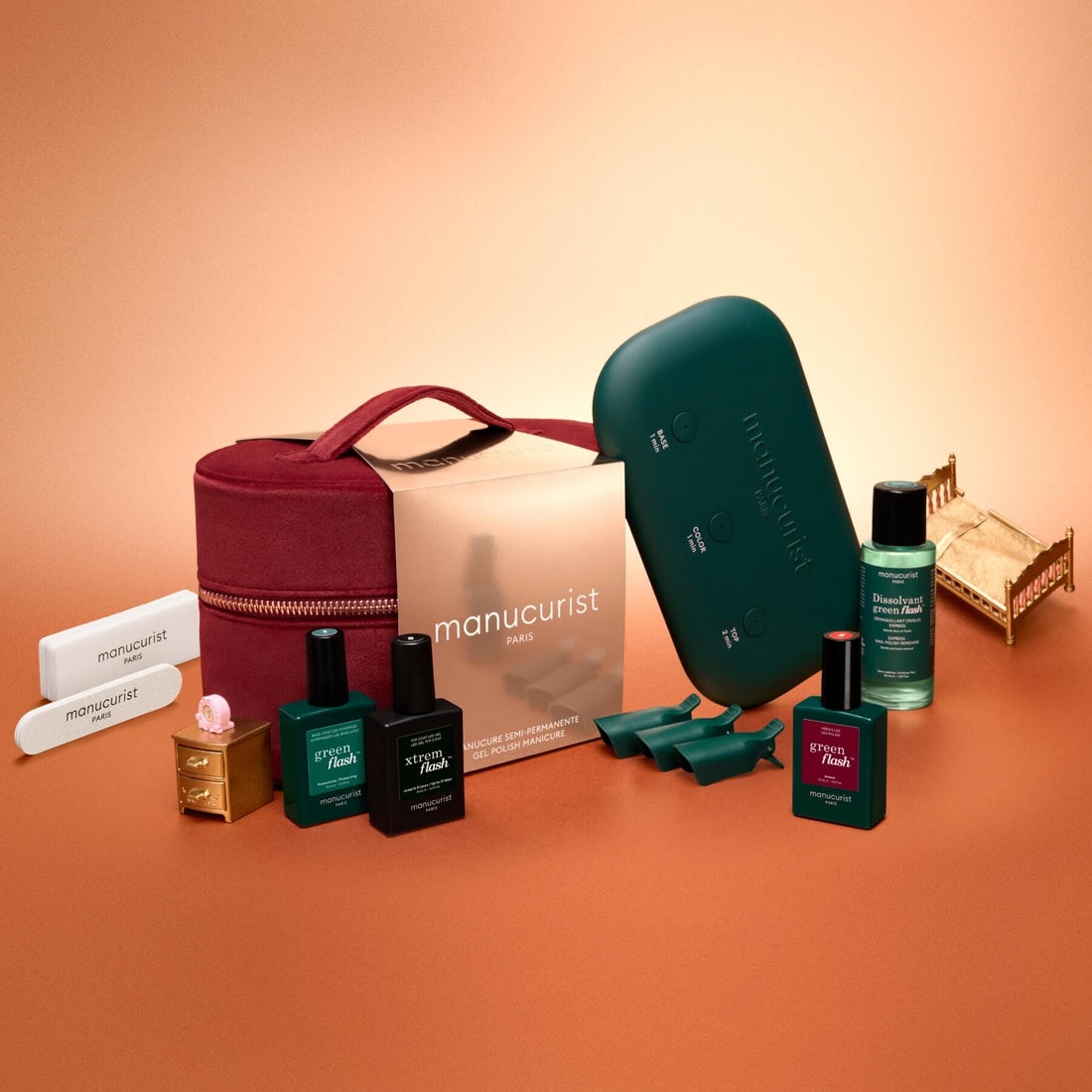 The Manucurist Green Flash™ Discovery Kit Gift Set includes nail polishes, a maroon zip pouch, nail files, a green UV lamp, remover, and accessories—beautifully arranged on a peach background—providing everything you need for long-lasting nails and a salon-style manicure at home.
