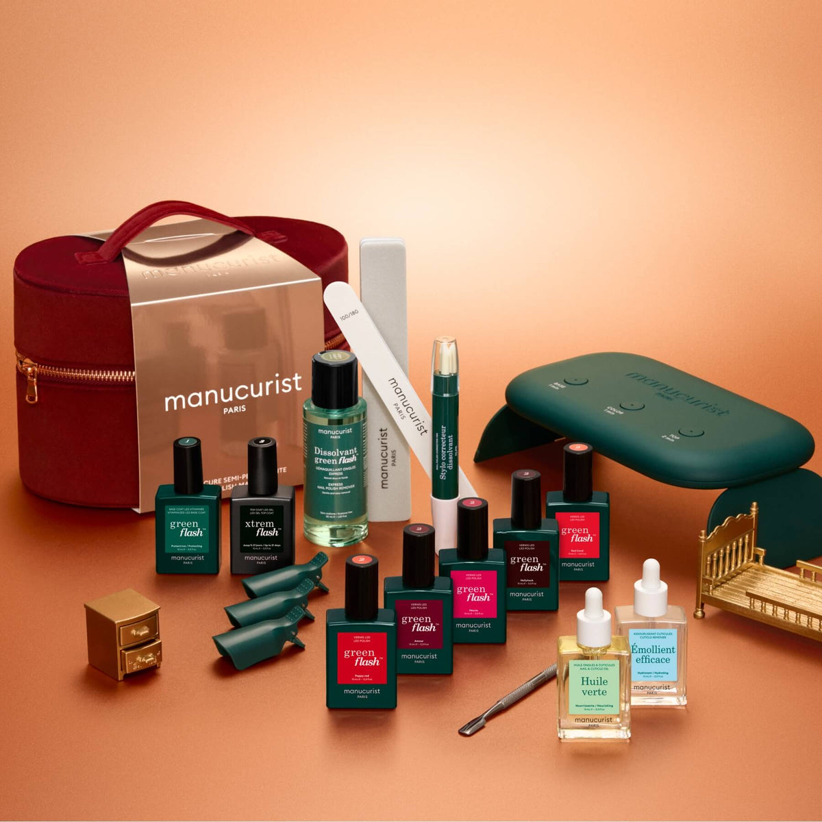 The Manucurist Green Flash™ Super Ultimate Kit Gift Set comes with Green Flash gel polish, nourishing oils, a nail file, a green LED lamp, remover, a velvet case, and essential manicure tools—all beautifully arranged on a warm brown background.