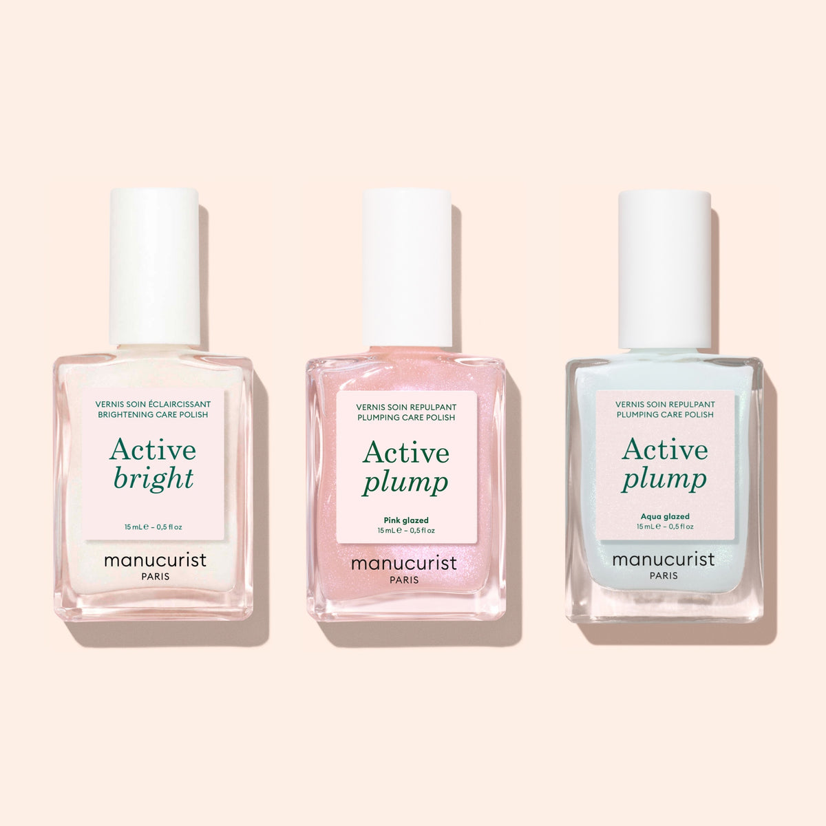 Three bottles of Manucurist nail polish are side by side on a light background, each with a white cap. The labels read: Active bright, Active plump (pink), and Active™ Plump Aqua Glazed (blue), showcasing this collagen nail polish collection designed for hydrated nails and volumizing nail care.