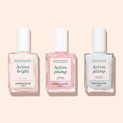 Three bottles of Manucurist nail polish are side by side on a light background, each with a white cap. The labels read: Active bright, Active plump (pink), and Active™ Plump Aqua Glazed (blue), showcasing this collagen nail polish collection designed for hydrated nails and volumizing nail care.