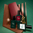 Three green bottles labeled Customizable Trio by Manucurist are displayed alongside a small gold teapot set, a gold statuette, and geometric props against a green background, creating a stylish, modern arrangement.