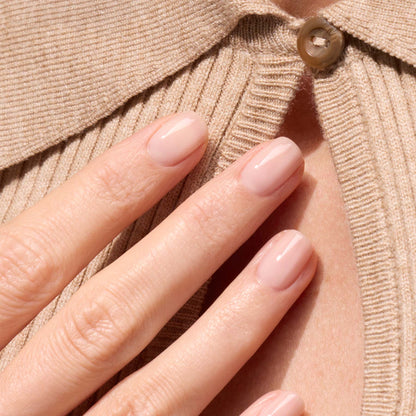 A hand with neatly manicured Manucurist Pale Rose nails rests on a beige ribbed sweater with a buttoned collar.