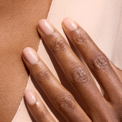 Gros plan sur une main aux ongles courts et ovales vernis avec Pale Rose de Manucurist, un vernis rose pastel translucide, posée sur un tissu beige clair et dévoilant une manucure élégante et naturelle.