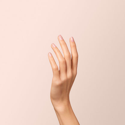 Une main aux ongles soigneusement manucurés, vernis avec le Hortencia rose translucide de Manucurist, est levée sur un fond beige doux.