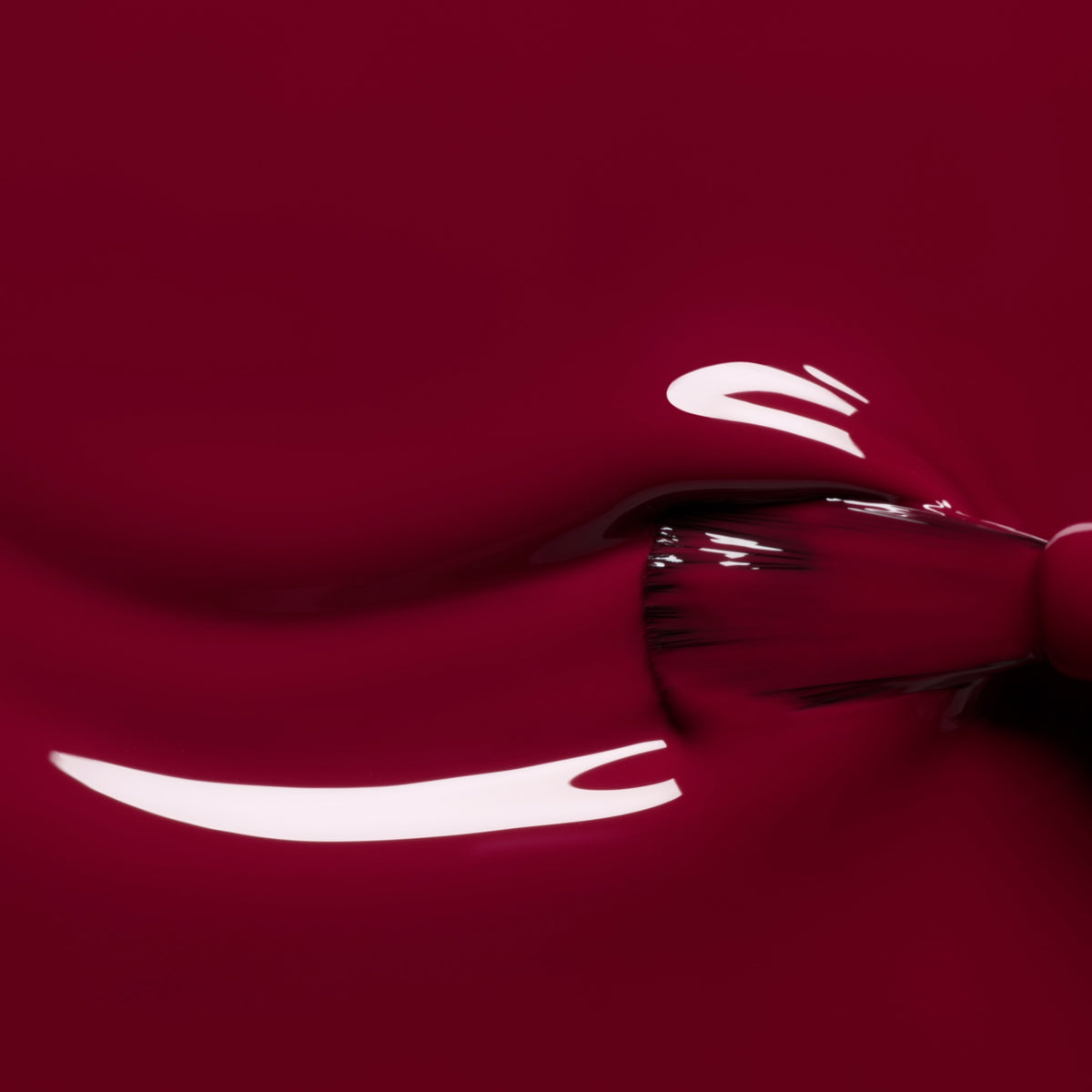 A close-up of a brush applying Manucurist’s Amour nail polish from the Green™ range, with shiny light reflections visible on the smooth burgundy surface.