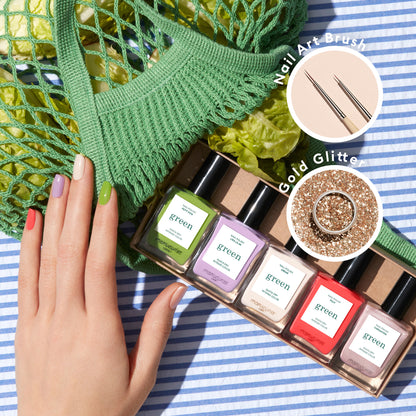 A hand with multicolored nails rests on a striped cloth next to five green-label Manucurist "Glitter in Love" nail polish bottles, biodegradable glitter, thin nail art brushes, and a green mesh bag of lettuce.