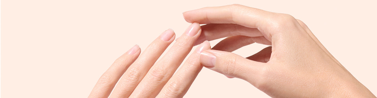 A close-up of two hands with well-manicured, natural nails gently touching each other against a light beige background.