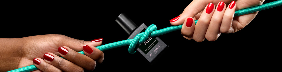 Two hands with red-painted nails hold a green rope tied around a black bottle, all set against a black background. The bottle appears to be nail polish.
